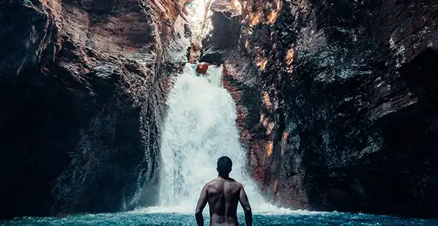 Un homme debout dans l’eau devant une cascade.
