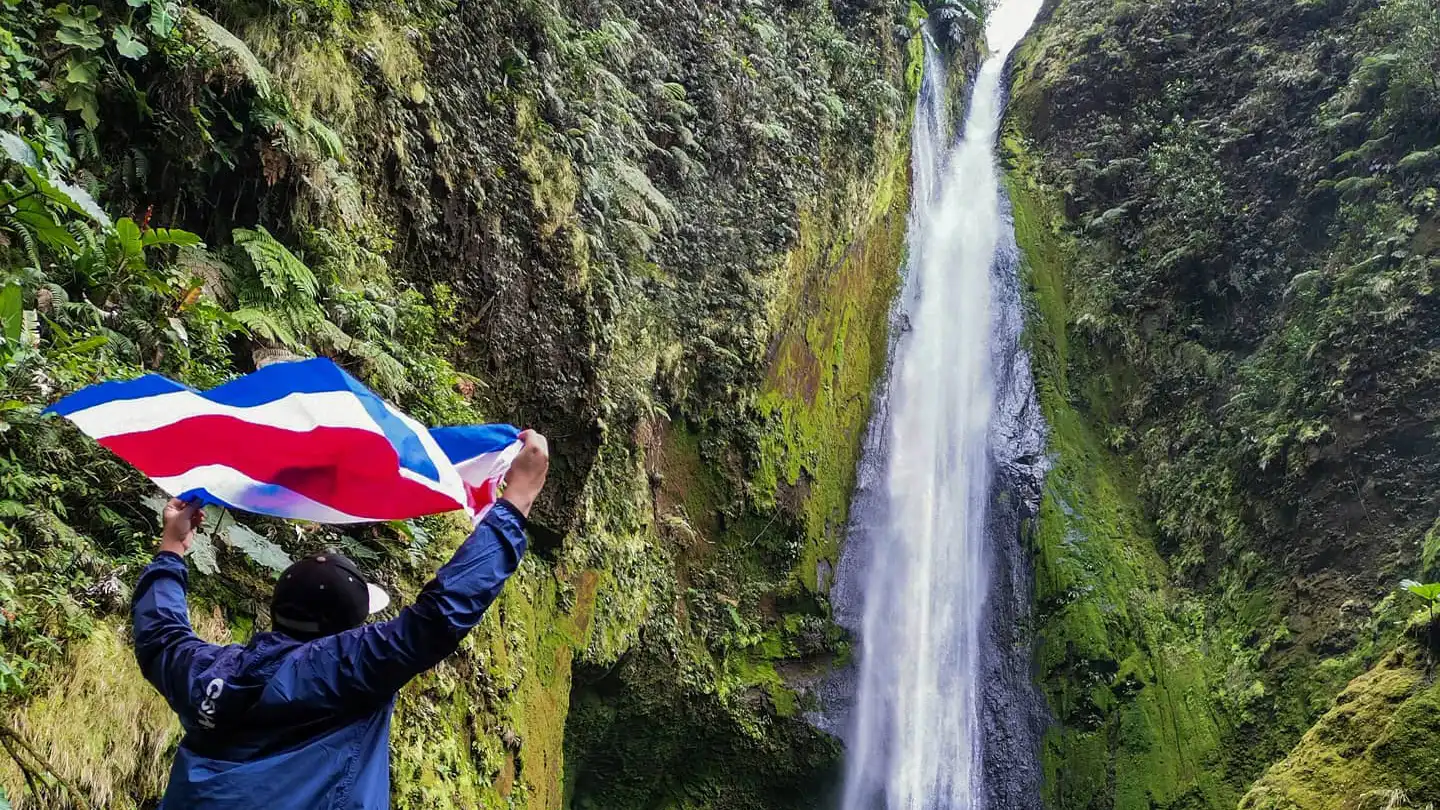 Un homme tenant un drapeau devant une cascade.