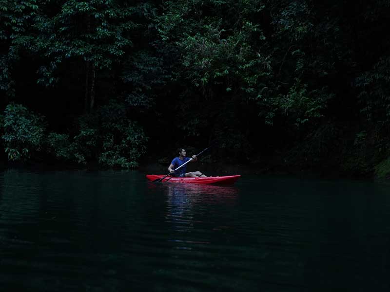 Un homme dans un kayak rouge pagaie dans l’eau.