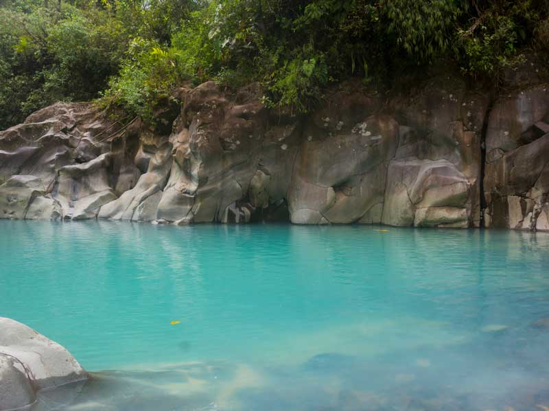 Un bassin d’eau bleue entouré de rochers et d’arbres.