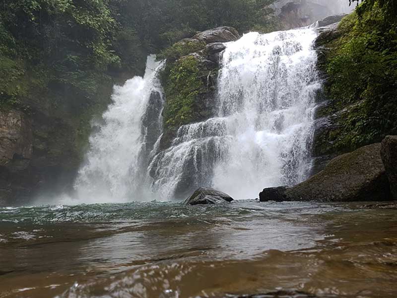 Un homme debout dans une rivière à côté d’une cascade.