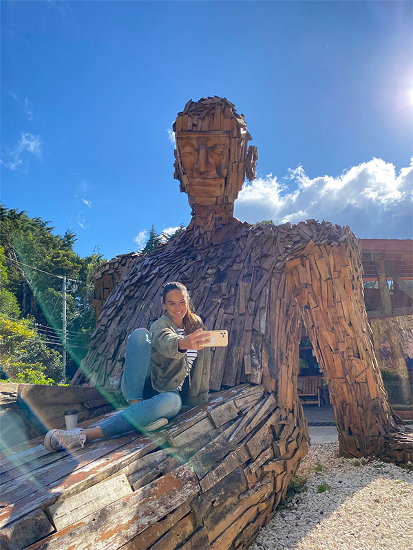 Une femme assise au sommet d’une sculpture en bois.