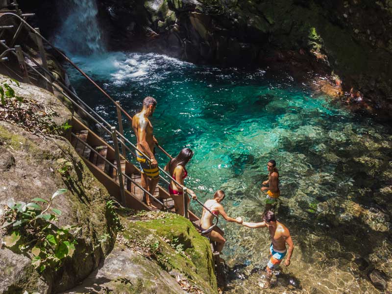 Un groupe de personnes debout au sommet d’une falaise à côté d’une chute d’eau.