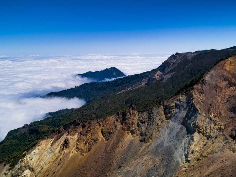 Une vue du sommet d’une montagne avec des nuages en dessous.