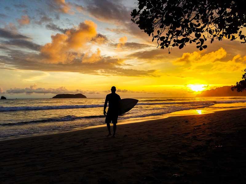 Un homme tenant une planche de surf debout sur une plage.