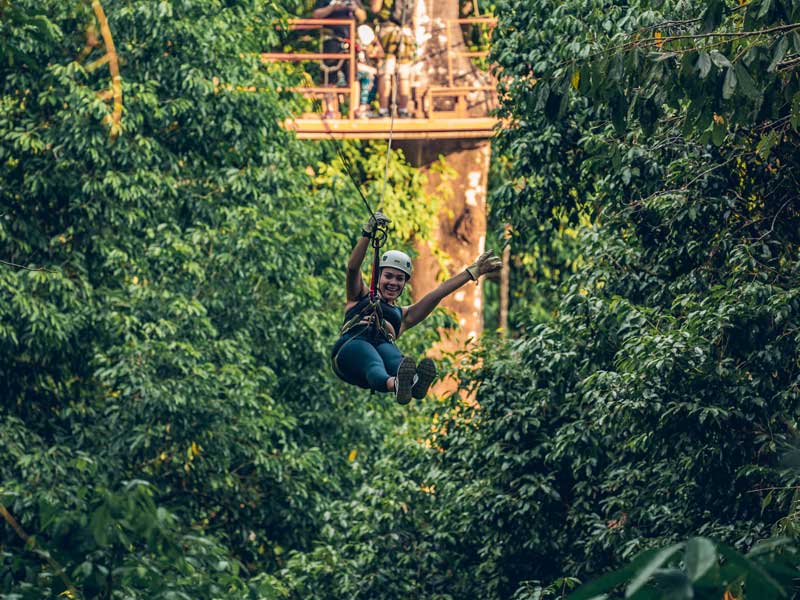 Une femme chevauchant une tyrolienne au milieu d’une forêt.