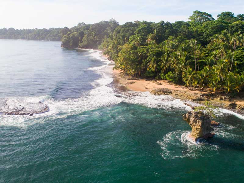 Une vue aérienne d’une plage avec un rocher au milieu de l’océan.