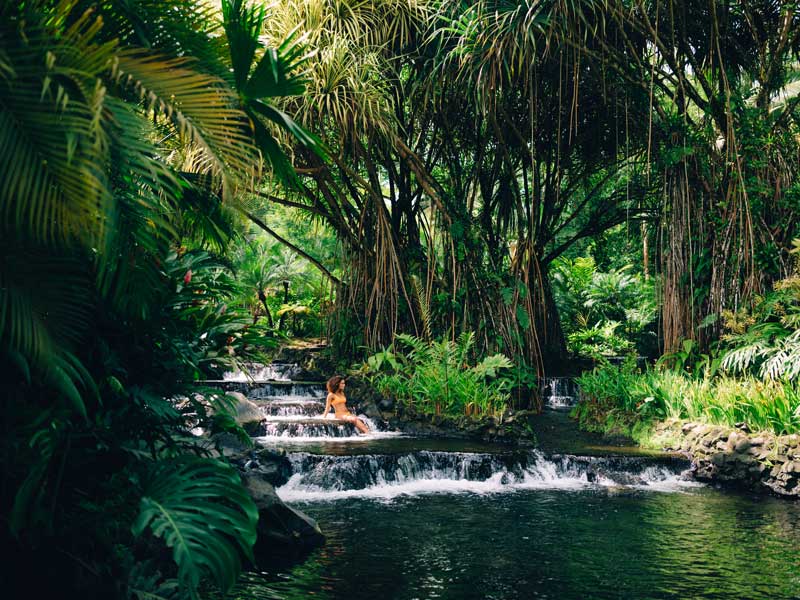 Une femme est assise sur une petite cascade dans la jungle.