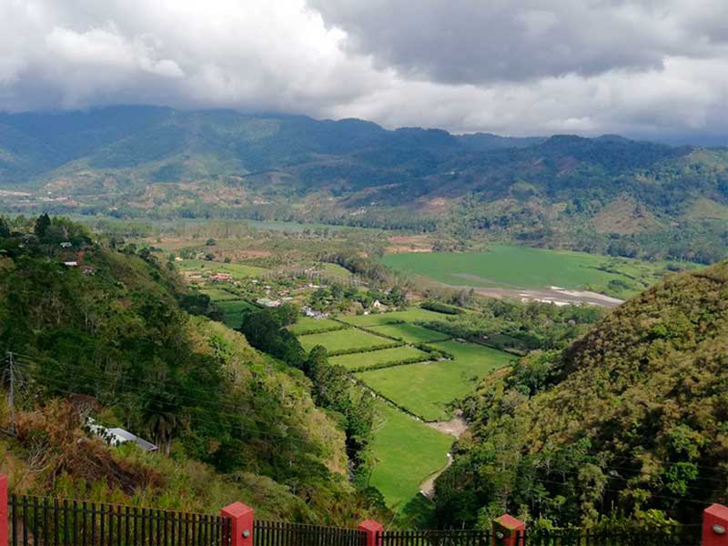 Une vallée verdoyante entourée de montagnes sous un ciel nuageux.