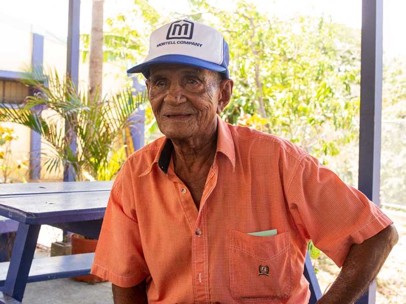Un vieil homme portant un chapeau assis à une table de pique-nique.