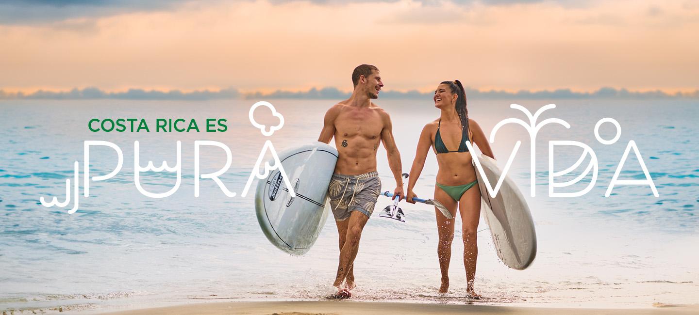 Couple marchant sur la plage avec des planches de surf et "pura vida» texte autour d’eux