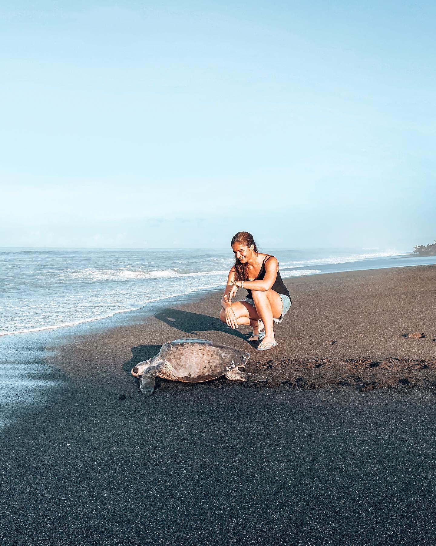 Une femme debout près d’une tortue sur une plage