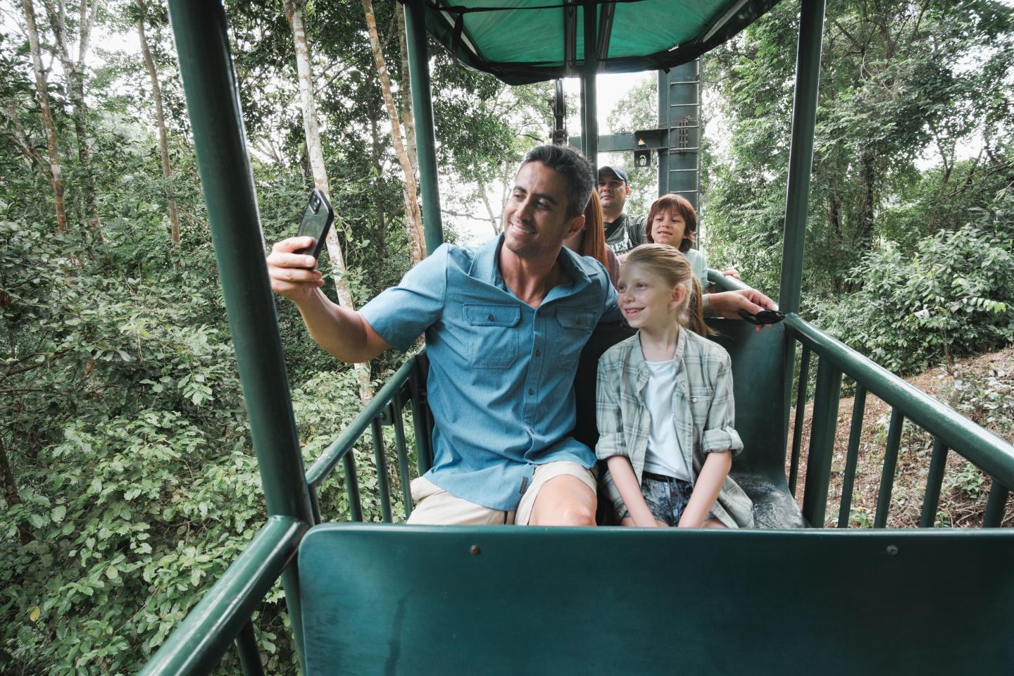 Famille prenant un selfie dans une gondole en plein air au-dessus de la canopée de la forêt tropicale.