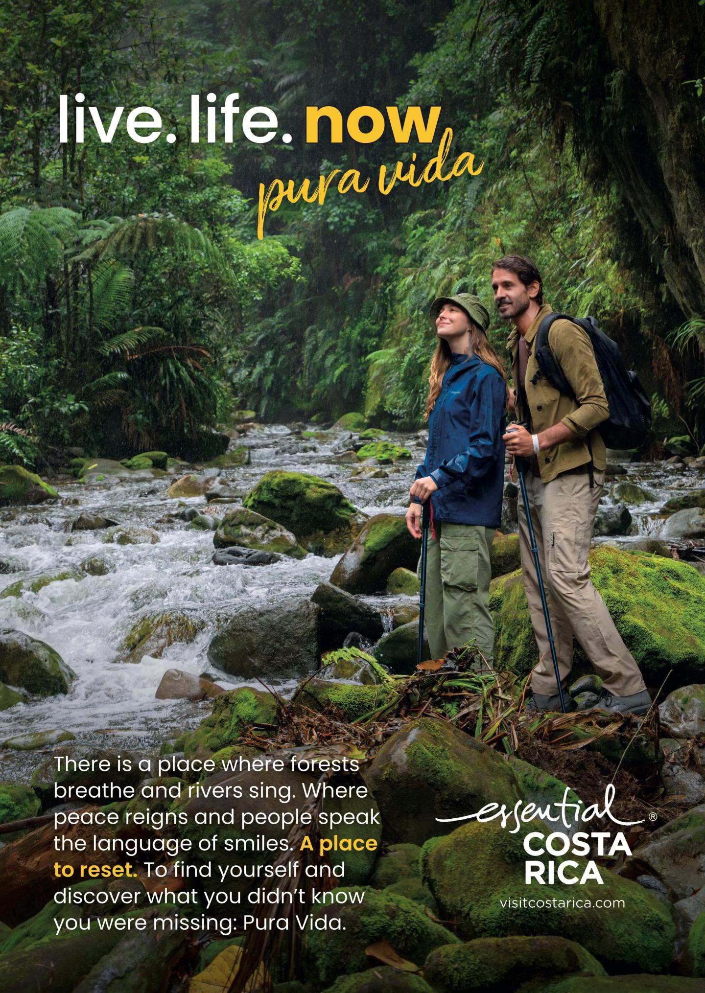 Publicité montrant deux randonneurs debout sur des rochers couverts de mousse au bord d’une rivière dans une forêt tropicale luxuriante. Titre : « vis.vie.maintenant » et «pura vida”. Le texte décrit des forêts qui respirent, des rivières qui chantent, et une chance de se réinitialiser. Logo : « esencial Costa Rica", visitcostarica.com.
