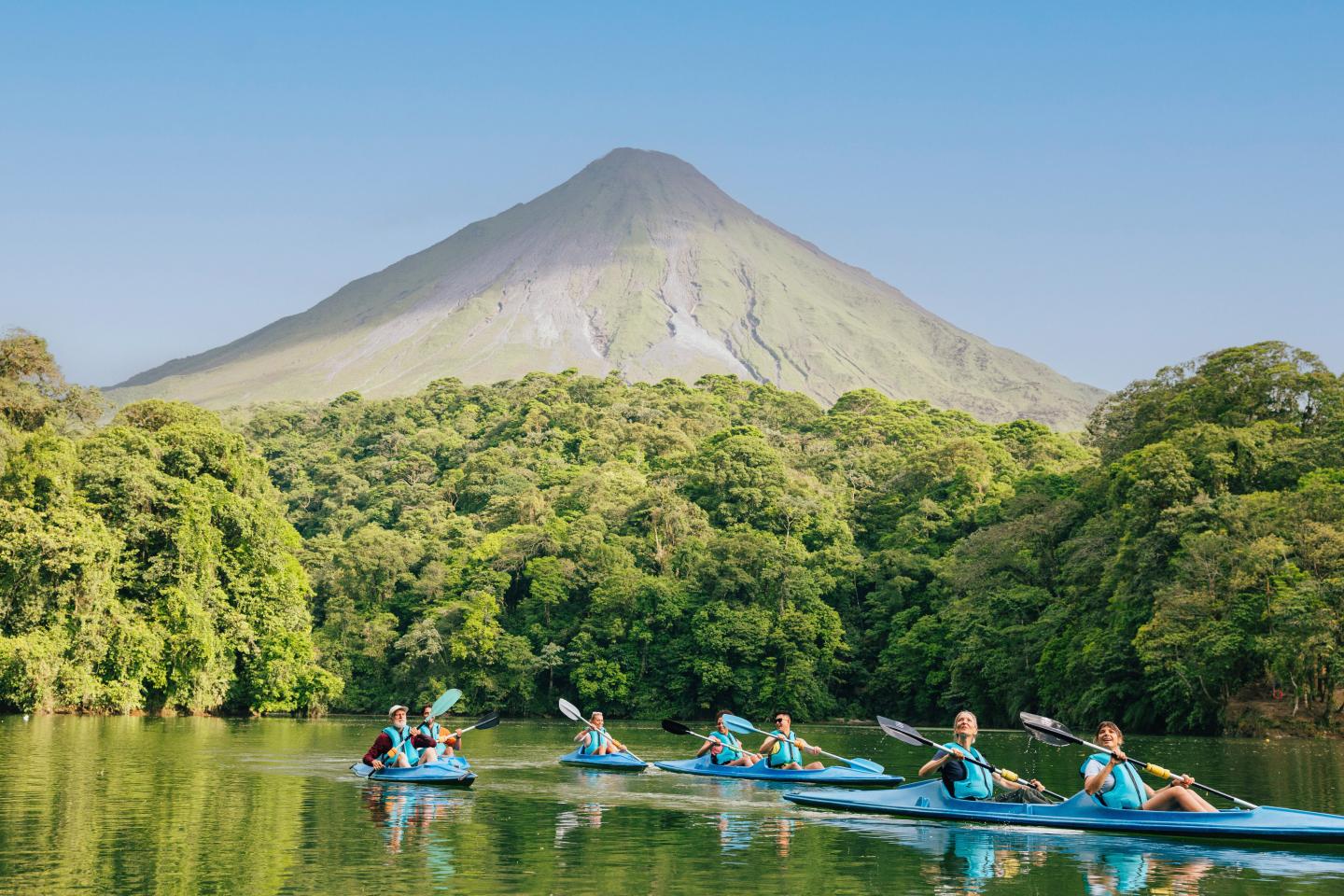Kayak en groupe sur un lac calme bordé de forêt tropicale, avec le volcan Arenal qui s’élève en arrière-plan.
