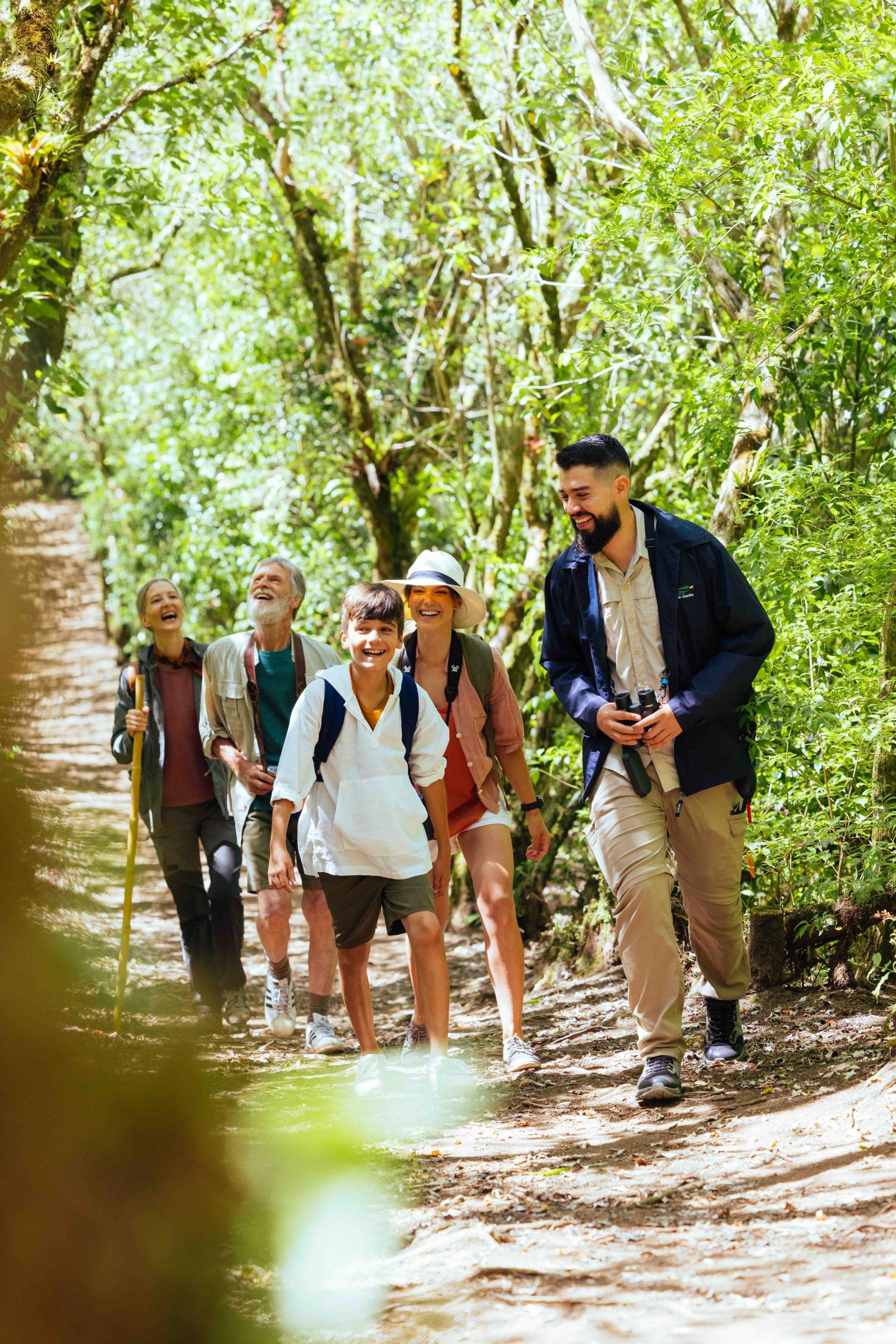 Un petit groupe de voyageurs marche le long d’un sentier forestier ombragé avec un guide.